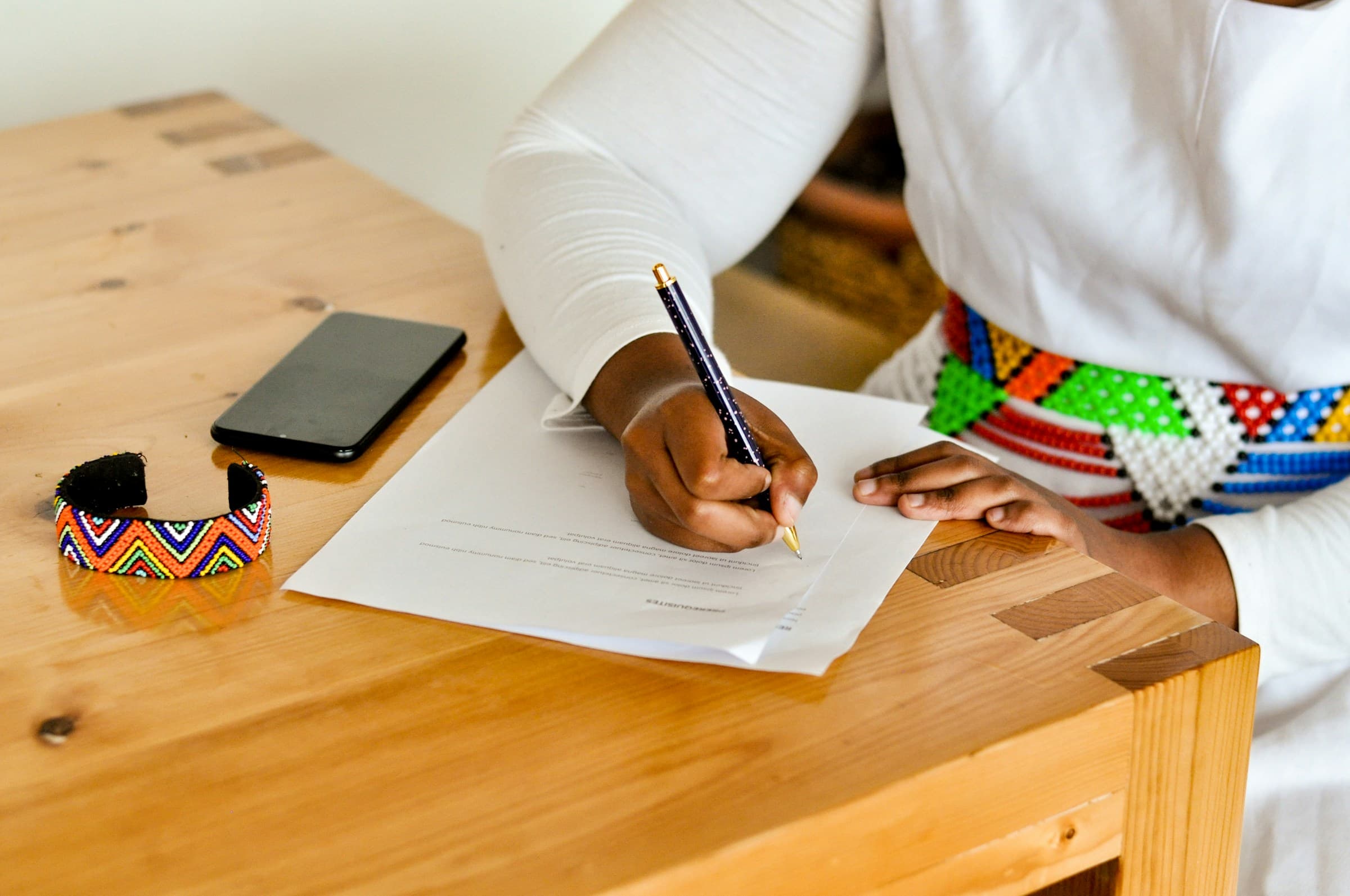 Woman in traditional African attire signing a document at a wooden desk