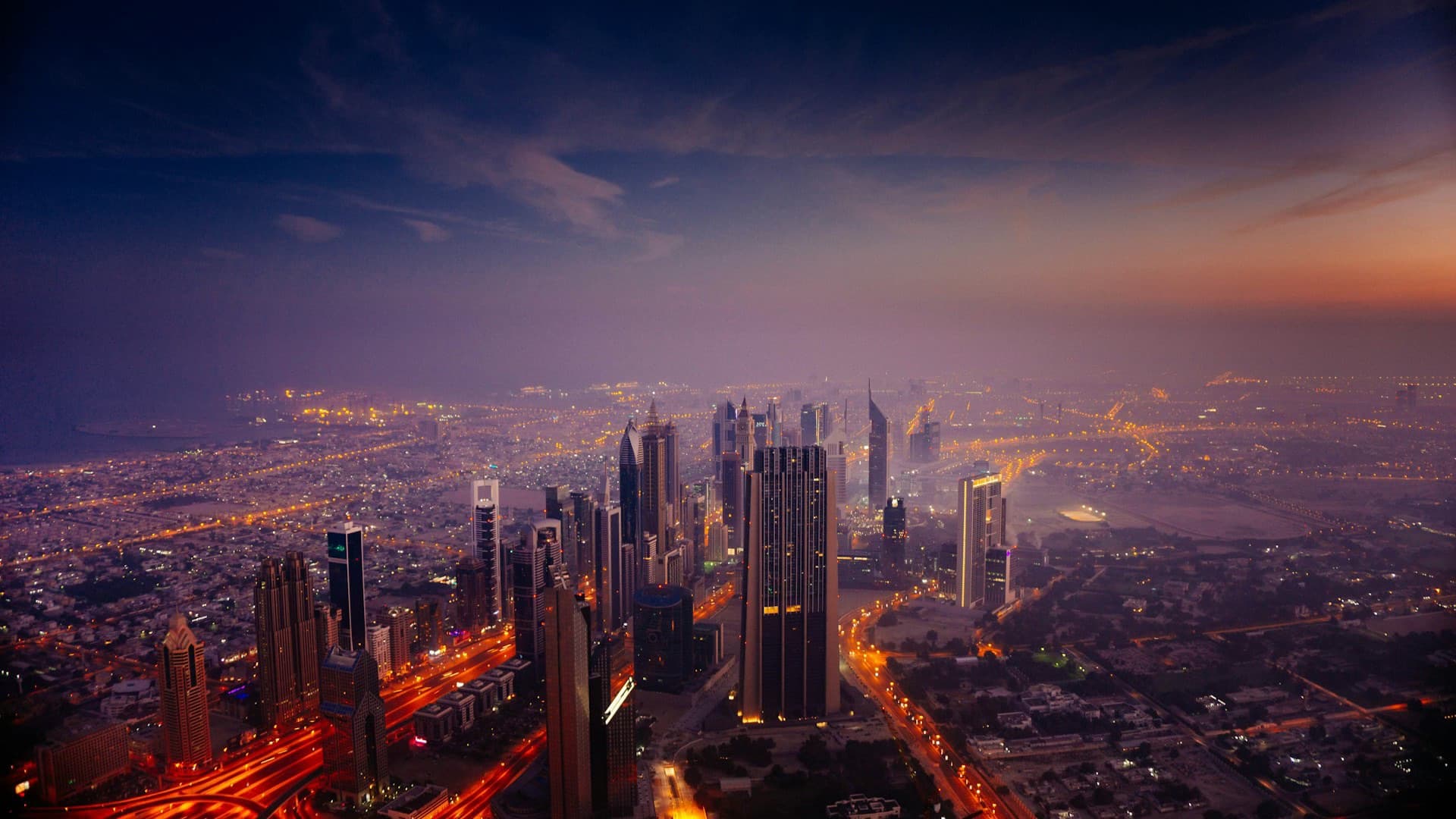An aerial view of a city skyline at dusk with lights coming on.