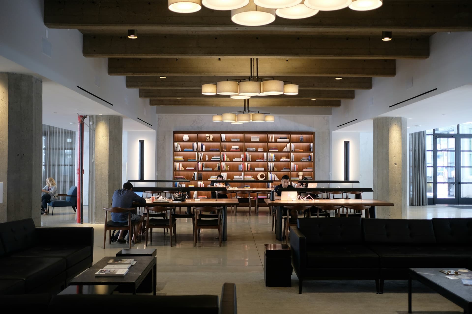 A modern library lounge with people working at long tables.